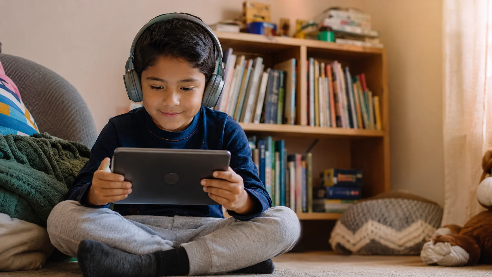Niño ecuatoriano de unos 7 años usando auriculares frente a una tablet con una aplicación de aprendizaje de inglés interactiva, con expresión de concentración y disfrute en su habitación