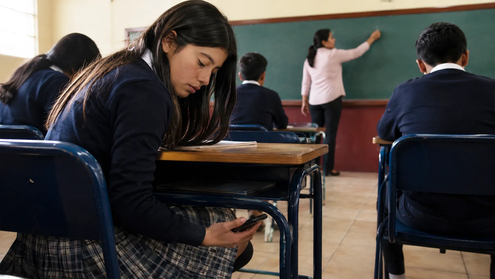 Adolescente ecuatoriano usando el celular en un aula escolar moderna